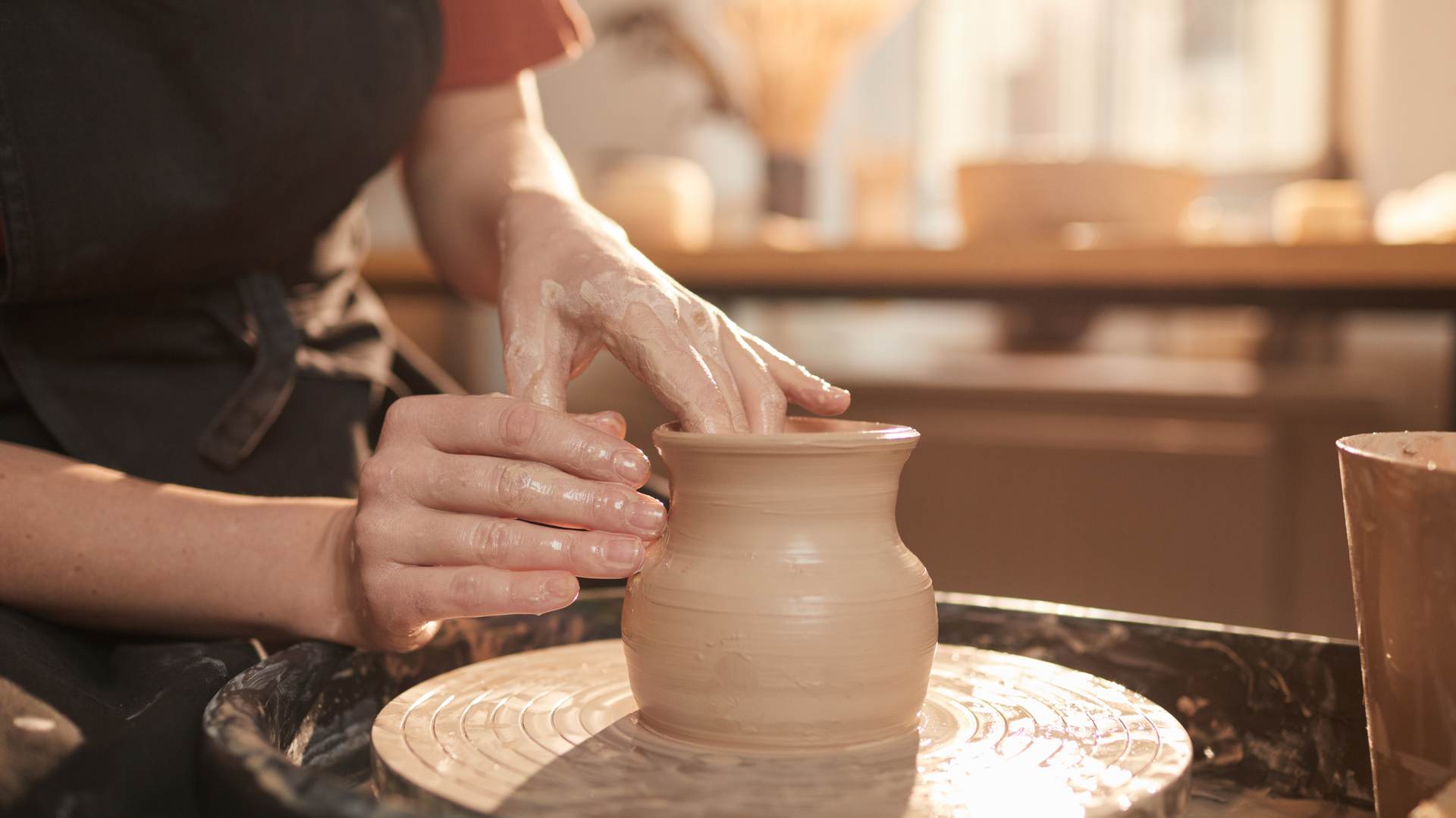 Hands shaping wet clay on a pottery wheel, sunlit workshop table at Craftorium Pattaya