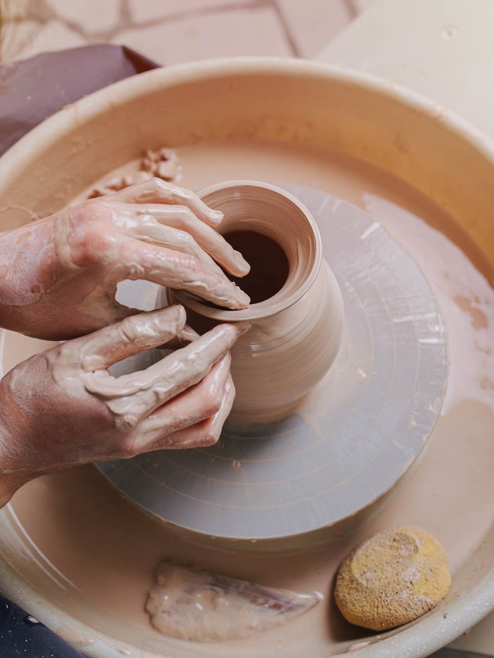 A hand shaping a clay vase on a pottery wheel at Craftorium